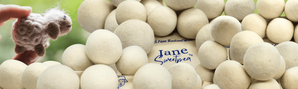 Pile of wool dryer balls with visible Jane Sweetpea branded pouch in background
Hand holding a felted sheep toy over a pile of wool dryer balls with green outdoor background